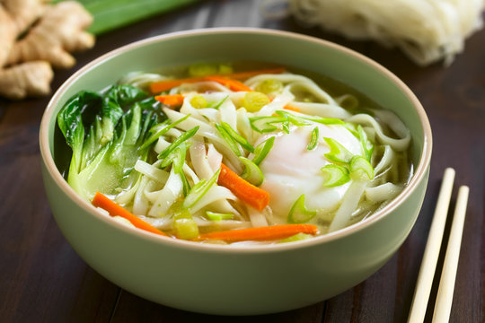 Vegetarian Asian rice noodle soup with bok choy, carrot, spring onion and a poached egg, photographed with natural light (Selective Focus, Focus in the middle of the soup)