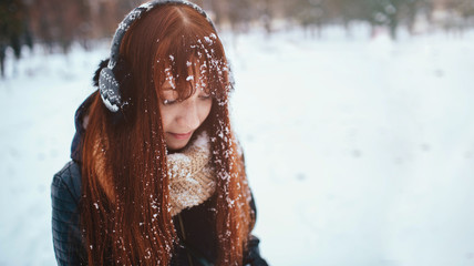 Winter. Woman with red hair wearing ear muffs . She is looking down. Snow on the 