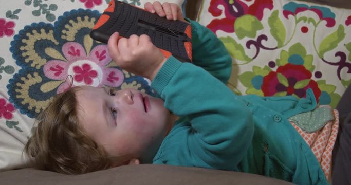 Little girl holding and using a tablet computer whilst lying down