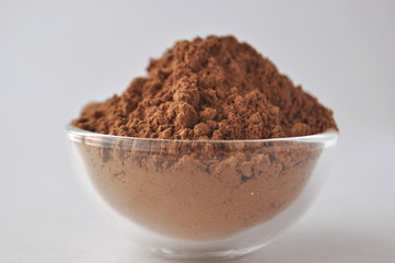 Raw cocoa (Theobroma cacao) powder in a glass bowl, closeup on white background
