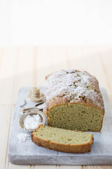 Japanese green Matcha tea cake on a cutting board. the cake is listed with confectioners sugar. 