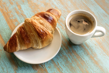 Cup of dark coffee with croissant, on wooden table
