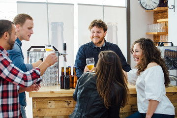 Five people laughing while drinking beer in bar