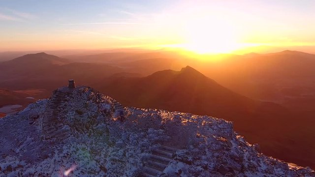 Stunning aerial shot of a man with his dog on a cold mountain summit at sunrise.