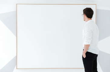 Side view of man wearing eyeglasses standing near big board.