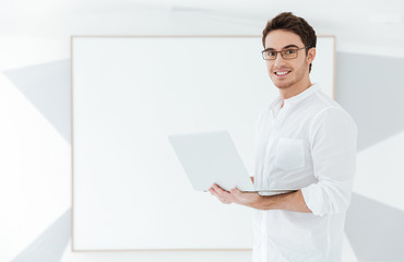 Image of cheerful man using laptop computer near big board.