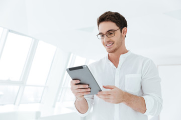 Happy young man standing near window while holding tablet computer.