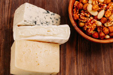 Delicious variety of cheese and nuts on old dark wooden table Top view