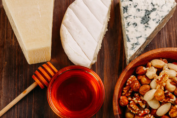 Delicious variety of cheese and nuts with honey on old dark wooden table Top view 