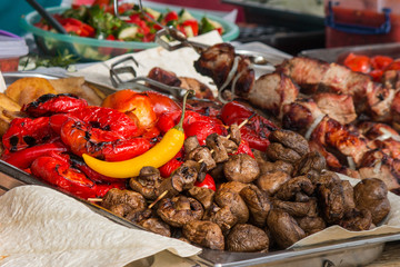 Pan with grilled vegetables, pepper, mushrooms, grilled meat on skewers,.., pita, salad on background. Food festival on open air