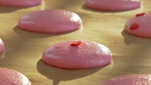 Dressing for macaroon dough elements in the shape of a heart. The shadow of the sunlight on the parchment paper. Confectioner decorate macaroon edible hearts. Treats for Valentine's Day.