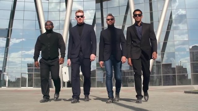 Dolly shot with slow motion of Caucasian, African and Latino mafia men in black suits and sunglasses walking towards camera