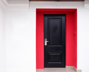 The modern entrance door of dark color placed in a building facade which is painted in red and white colors