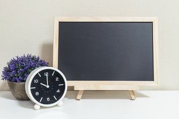 Closeup alarm clock for decorate show 10 o'clock with wood black board on white wood desk and cream wallpaper textured background , selective focus at the clock