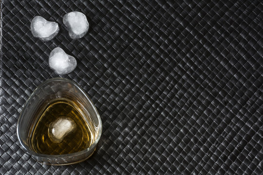 Glass of bourbon with ice on black leather background