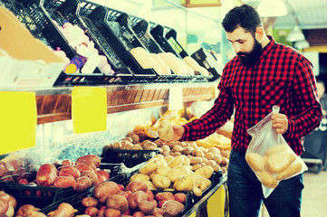 Smiling healthy man seller showing potatoes in grocery shop