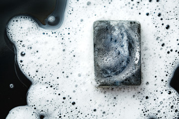 Black coal bar of soap in foam on dark