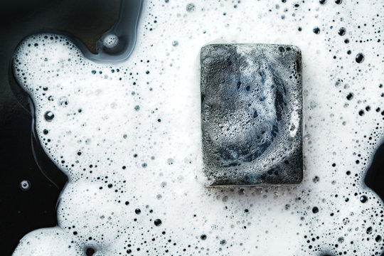 Black Coal Bar Of Soap In Foam On Dark