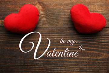Be my Valentine inscription on the wooden background with two soft decorative hearts.