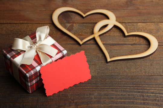 Gift box with decorative hearts on a wooden background.