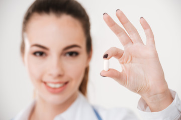 Happy pretty young woman doctor holding one pill