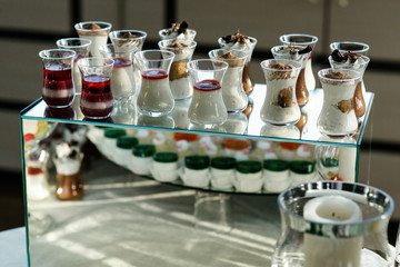 Glasses with tiramissu and other cold desserts stand on glass bo
