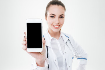 Cheerful cute young woman doctor showing blank screen mobile phone