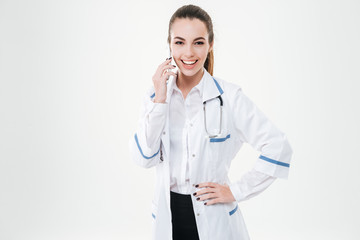 Smiling young woman doctor standing and talking on cell phone