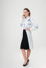 Smiling young woman doctor standing and talking on cell phone