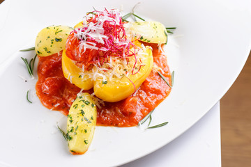 Stuffed vegetarian or vegan filled red paprika or bell pepper with spelt or brown rice and vegetables with cheese and fresh basil on a white plate on a kitchen background, closeup