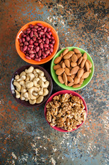 Set of variety of nuts. Almond, peanuts, walnuts and cashew in color ceramic bowls on a rusty background