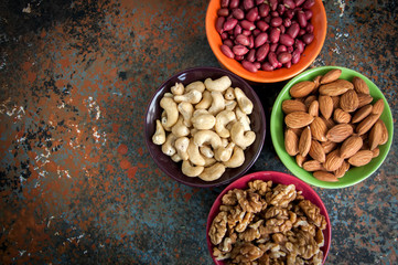 Set of variety of nuts. Almond, peanuts, walnuts and cashew in color ceramic bowls on a rusty background