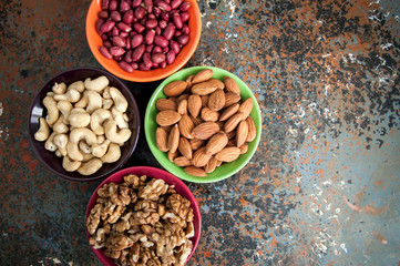 Set of variety of nuts. Almond, peanuts, walnuts and cashew in color ceramic bowls on a rusty background