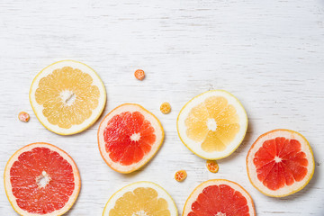Top view on cut red and yellow grapefruit and small citrus candies on white wooden background. Juicy and fresh fruit. Healthy eating concept.