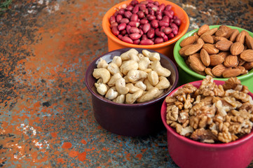 Set of variety of nuts. Almond, peanuts, walnuts and cashew in color ceramic bowls on a rusty background