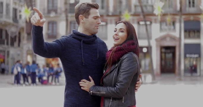 Attractive young man pointing out something in an urban square to his smiling girlfriend or wife  close up head and shoulders