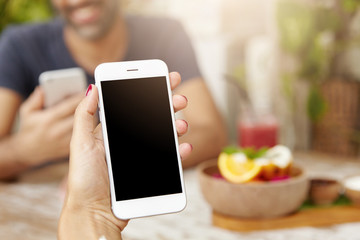 Cropped shot of Caucasian woman's hand holding generic mobile phone with blank copy space screen for your promotional content while enjoying free wi-fi at cafe during video call with her friend