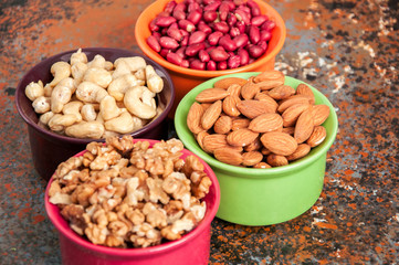 Obraz premium Set of variety of nuts. Almond, peanuts, walnuts and cashew in color ceramic bowls on a rusty background