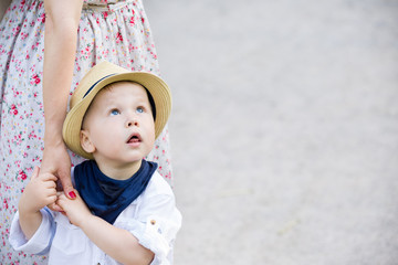 Portrait of a cute toddler boy on straw hat holding his mother's hand and looking at the sky. Adorable child with his mom walking in the park. Together. Childhood and lifestyle concept