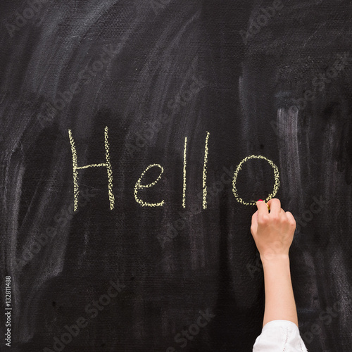 "Closeup of child's hand writing Hello word with chalk on the backboard