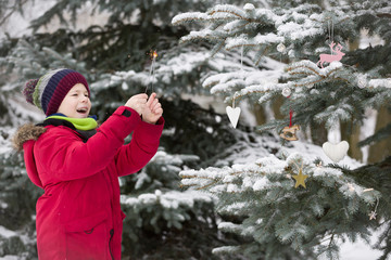 Fototapeta na wymiar Happy smiling kid boy decorating Christmas tree in winter snow park. Child having fun. Christmas celebration outdoors. Winter and holidays concept.