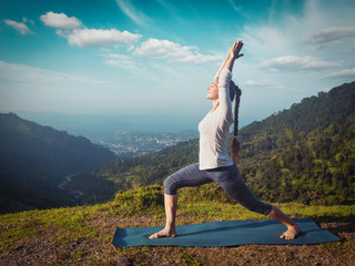 Woman doing yoga asana Virabhadrasana 1 - Warrior pose outdoors