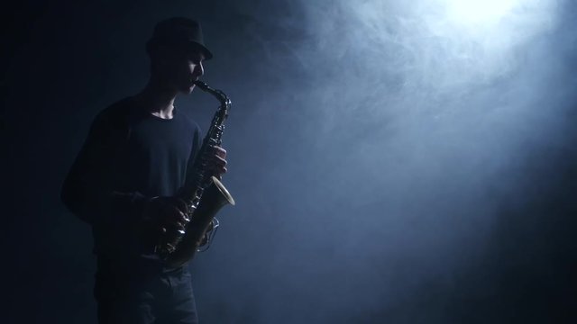 Jazzman performs composition on the saxophone. Smoke in the dark