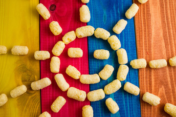 Sweet corn sticks in the form of the sun on multicolored wooden background