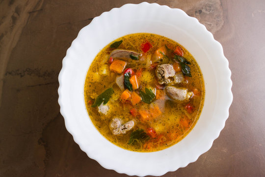 Vegetable soup with chicken giblets in a white bowl on a marble table
