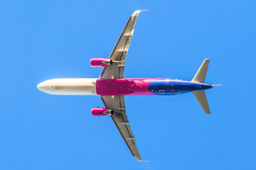 low angle view of a pink passenger commercial airplane isolated against the blue sky.