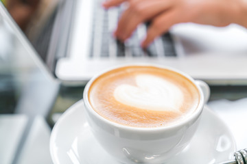 Closeup of  Latte Coffee art and woman hand typing on laptop key