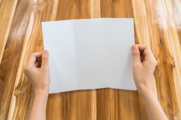 Obraz premium Women hand hold Trifold white template paper on wood texture .