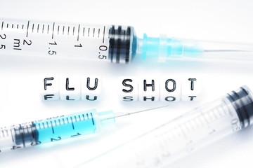 Flu shot text spelled with tiled plastic letters standing next to a syringe 