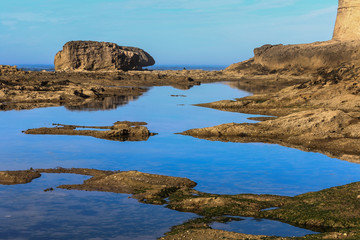 Küste von  Essaouira mit Steinen und  Wasserflächen in welchen sich der blaue Himmel spiegelt